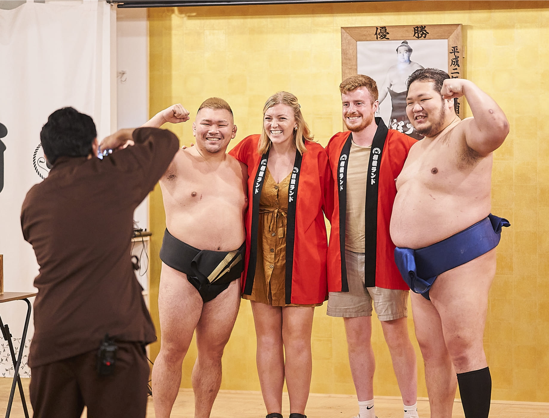 Guests in happi coats posing with sumo wrestlers